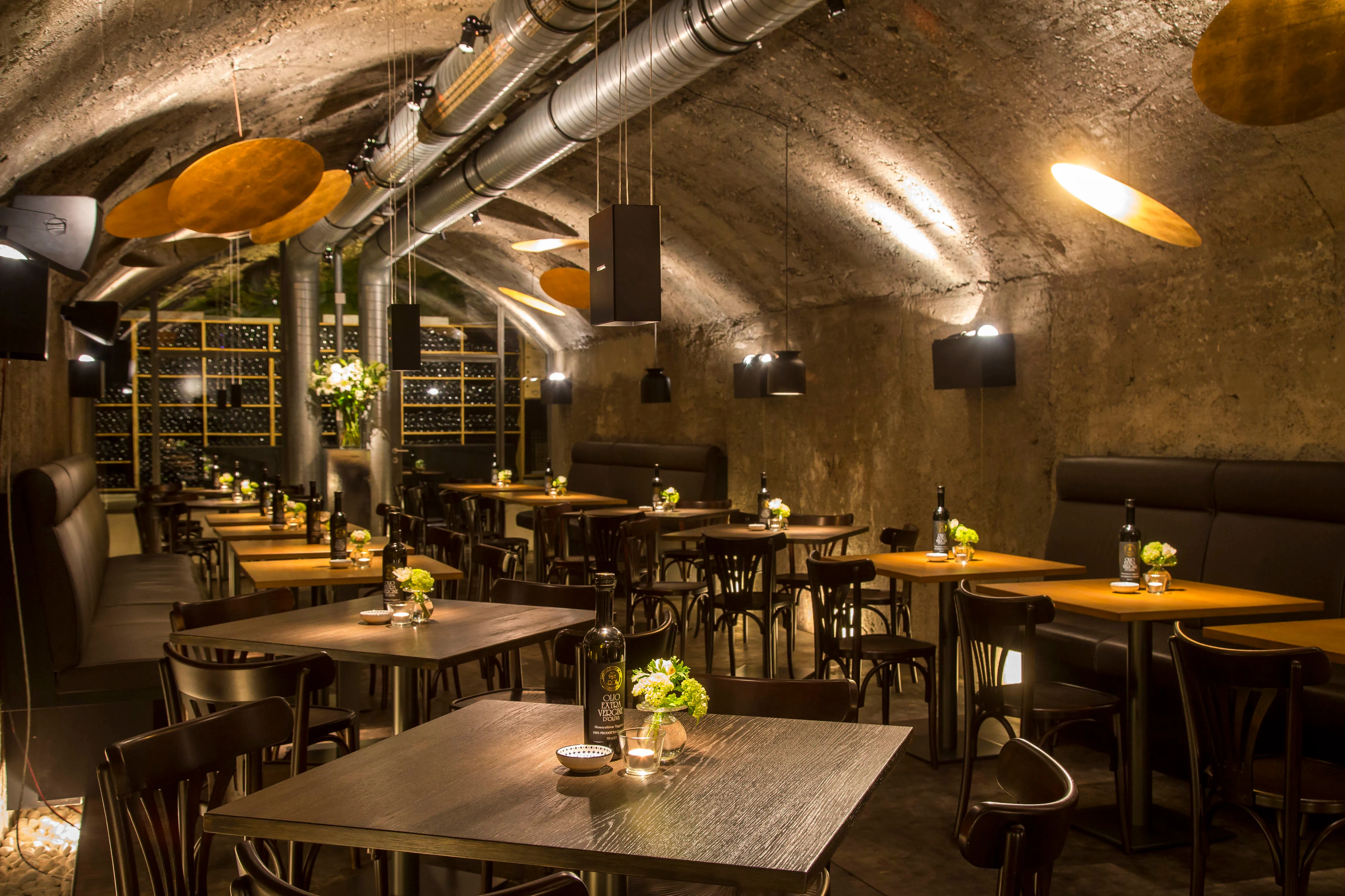 Bistro in der Kaverne im Mönchsberg, Restauranttische aus Holz mit Ölflasche, Blumen und Kerze. Industrieller Vibe